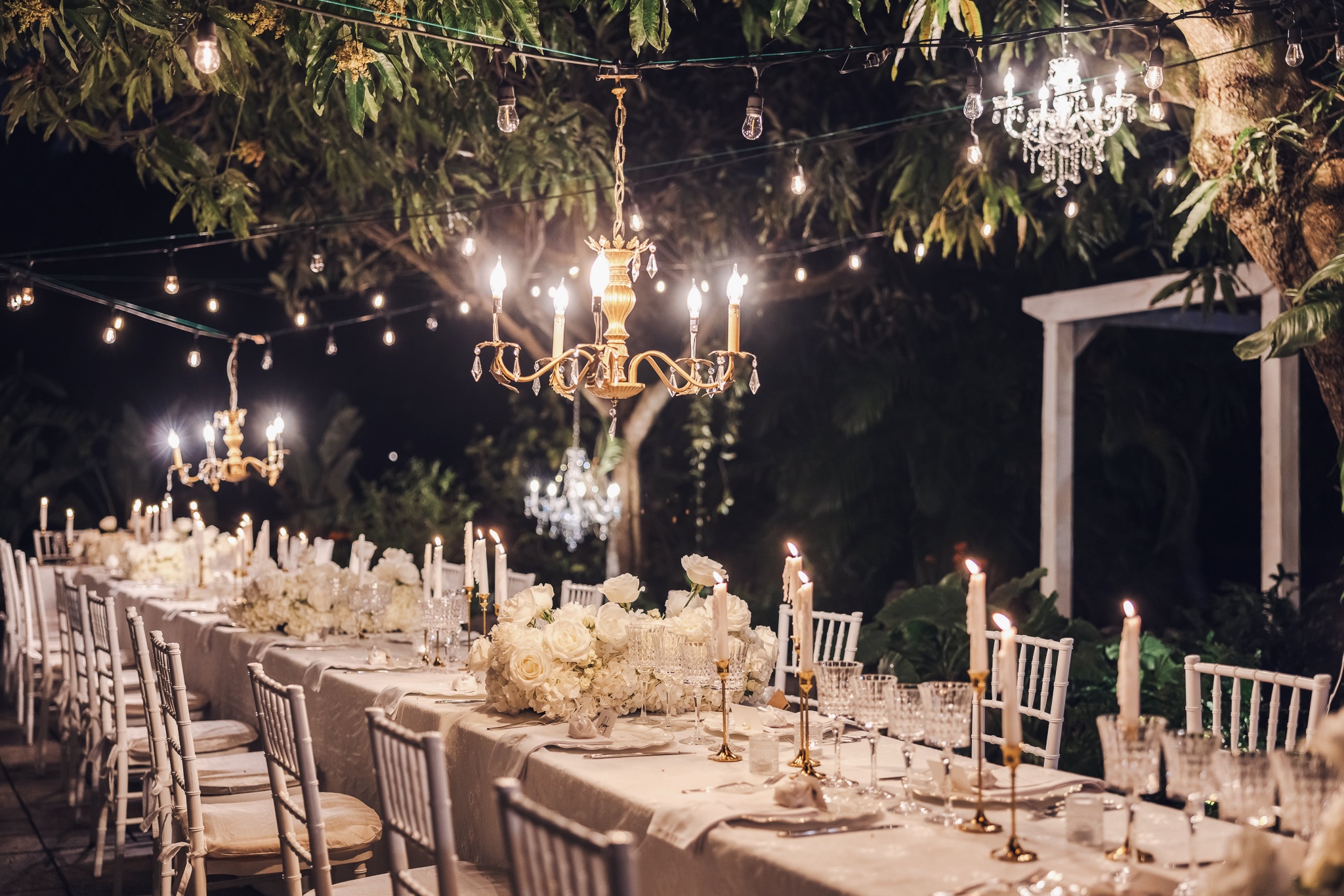 Candlelit outdoor reception beneath chandeliers and string lights